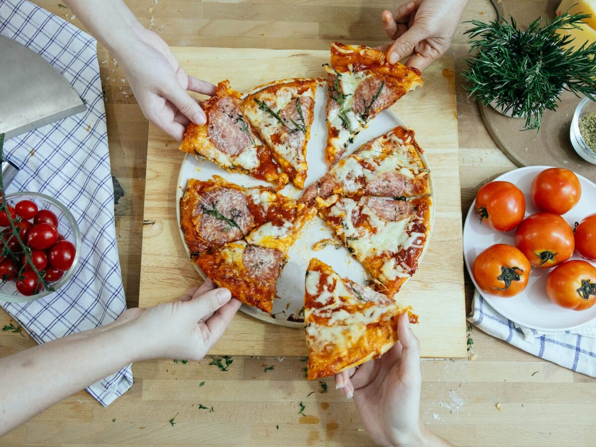 crop friends taking slices of delicious pizza from cutting board